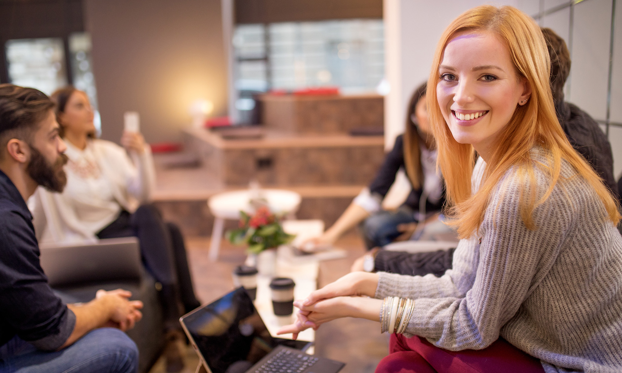 Young woman having a coffee with her collegues and looking into the camera smiling